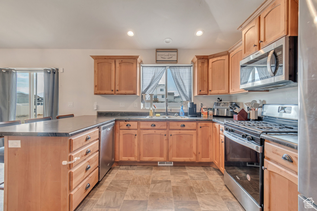 Kitchen with a peninsula, dark countertops, visible vents, stainless steel appliances, and a sink