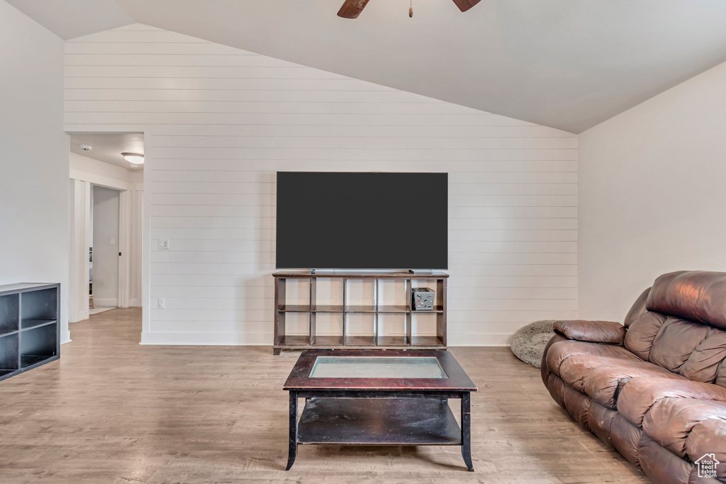 Living room with wood walls, vaulted ceiling, a ceiling fan, and wood finished floors