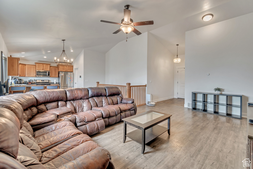 Living area featuring light wood-type flooring, baseboards, recessed lighting, high vaulted ceiling, and ceiling fan with notable chandelier