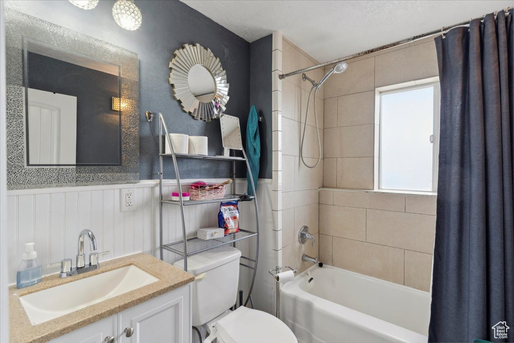 Full bath with vanity, wainscoting, shower / bathtub combination with curtain, and toilet