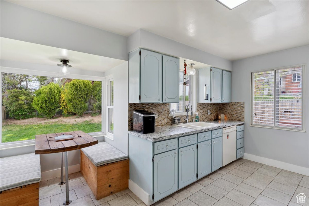 Kitchen with white dishwasher, light tile patterned flooring, a sink, baseboards, and decorative backsplash