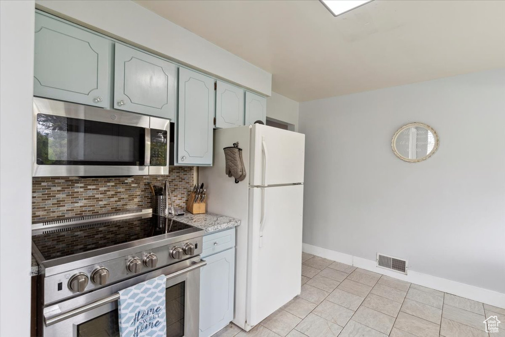 Kitchen with light stone countertops, appliances with stainless steel finishes, baseboards, decorative backsplash, and visible vents