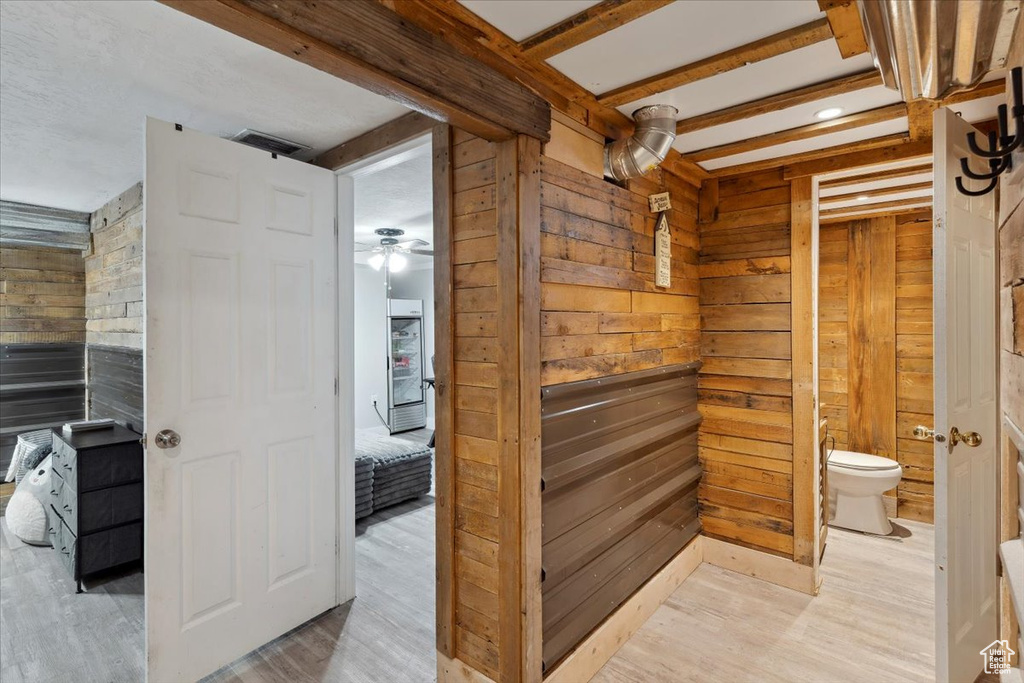 Bathroom featuring a ceiling fan, wood walls, beam ceiling, wood finished floors, and toilet