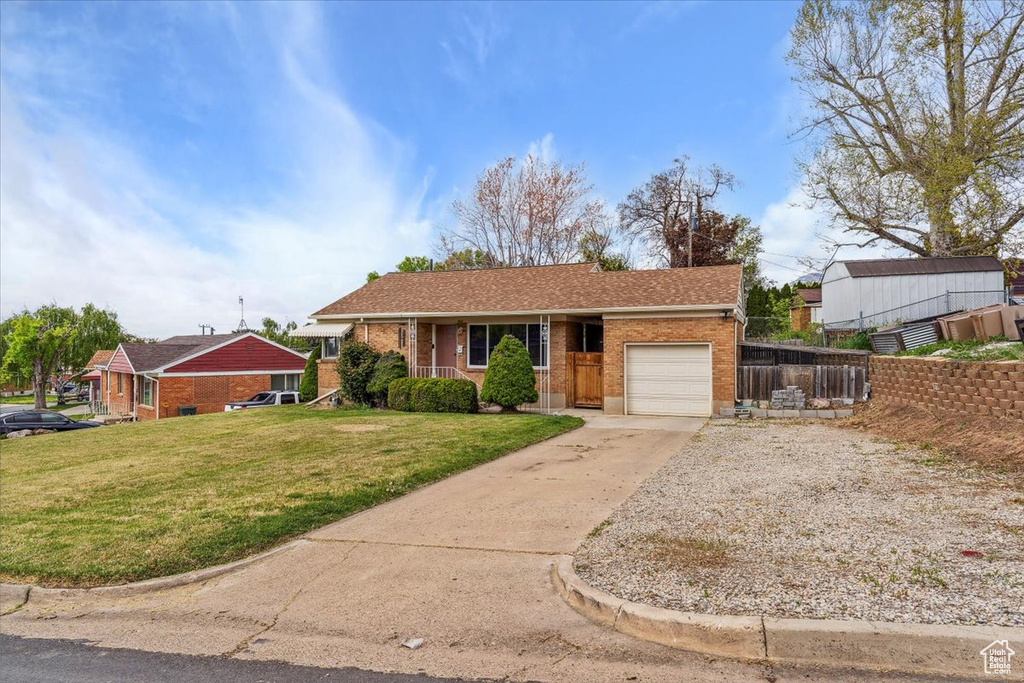 Ranch-style home with a front lawn, fence, brick siding, an attached garage, and driveway