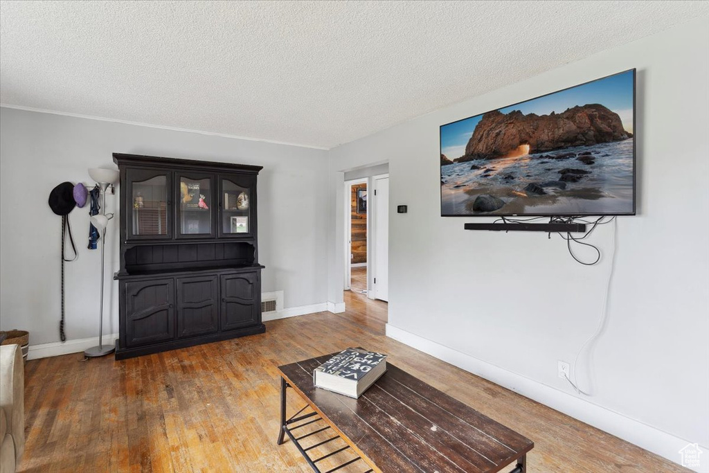 Living room with visible vents, baseboards, a textured ceiling, and wood finished floors