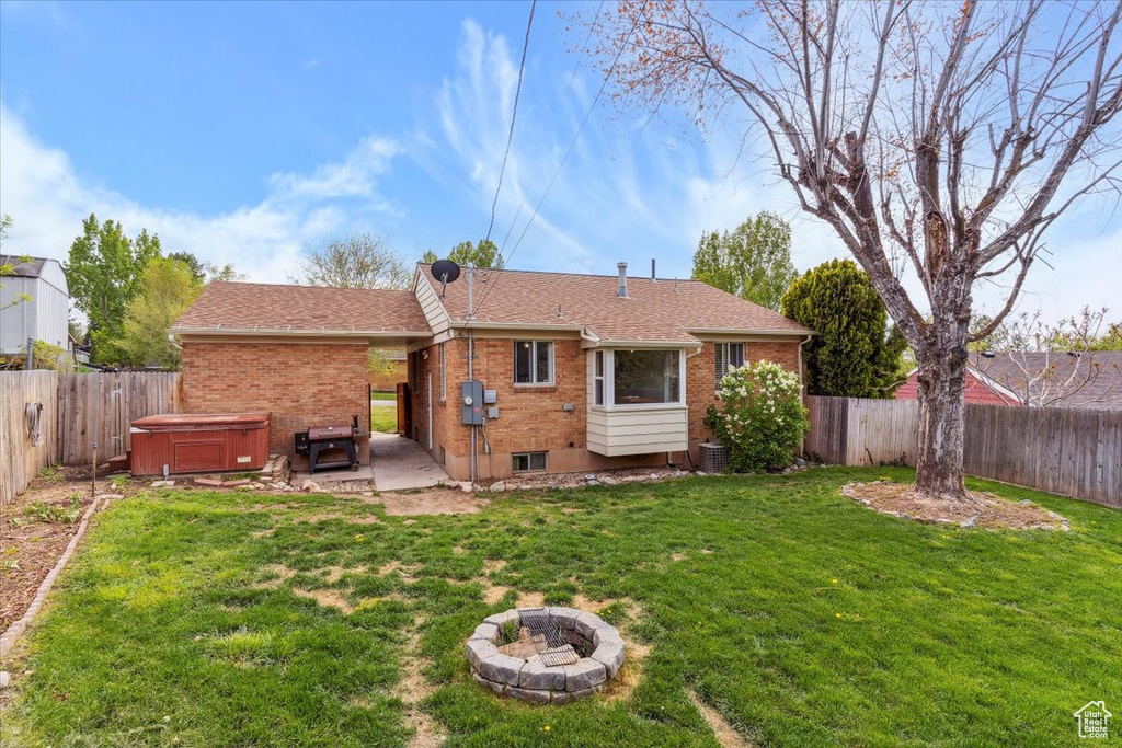Back of house with a hot tub, brick siding, a yard, and a fenced backyard