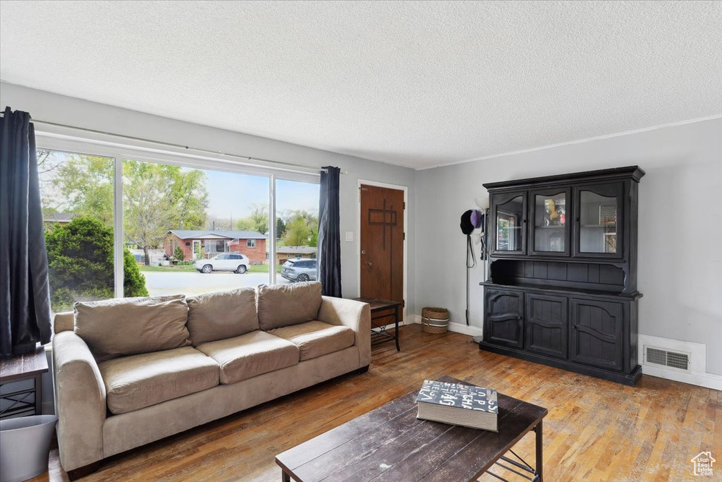 Living room featuring a textured ceiling, baseboards, wood finished floors, and visible vents