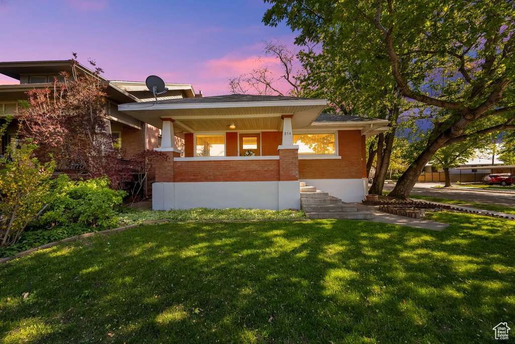 View of front of home featuring a yard, brick siding, and a porch