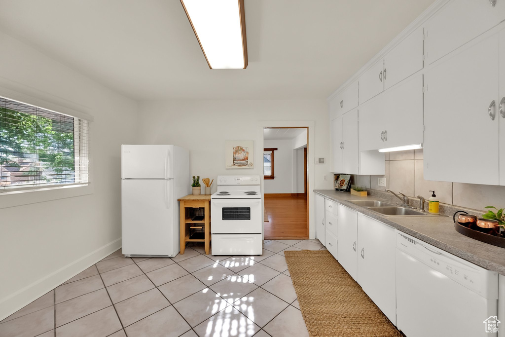 Kitchen featuring decorative backsplash, a sink, light tile patterned floors, white appliances, and white cabinetry
