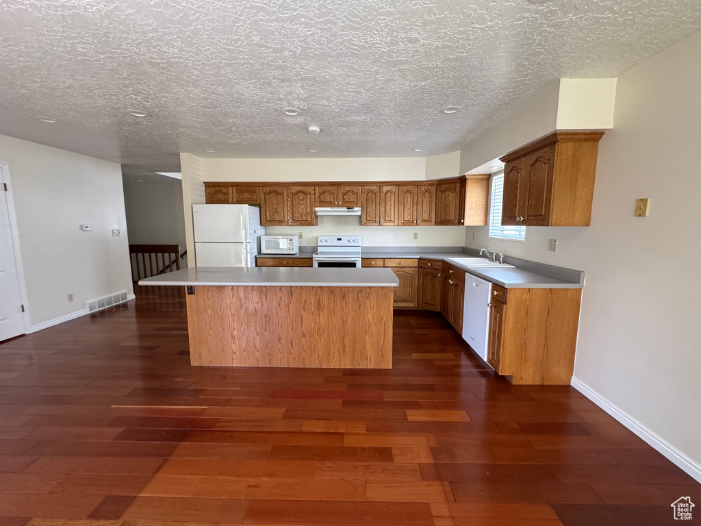 Kitchen featuring visible vents, a kitchen island, white appliances, dark wood-style floors, and under cabinet range hood