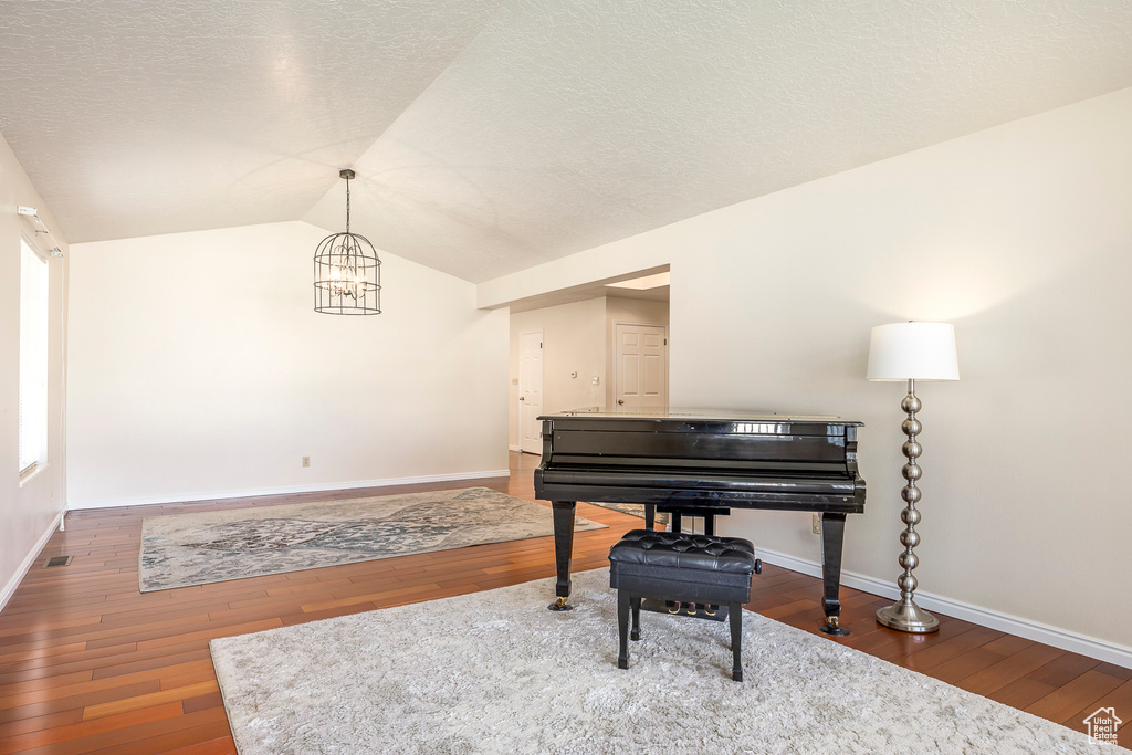 Living area with wood-type flooring, baseboards, an inviting chandelier, and vaulted ceiling