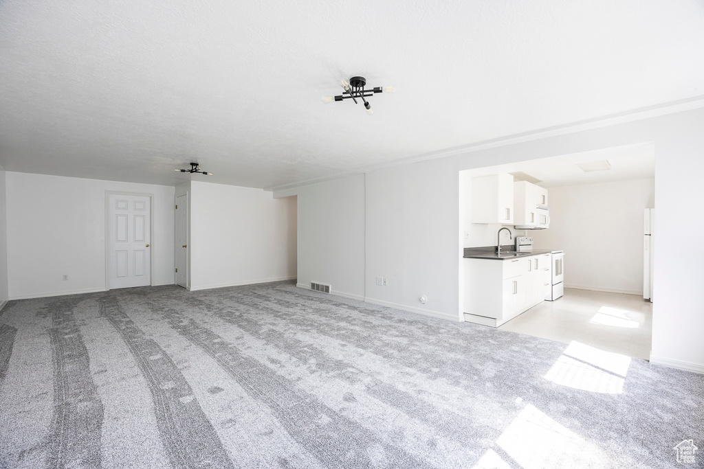 Unfurnished living room with light colored carpet, a sink, baseboards, and visible vents
