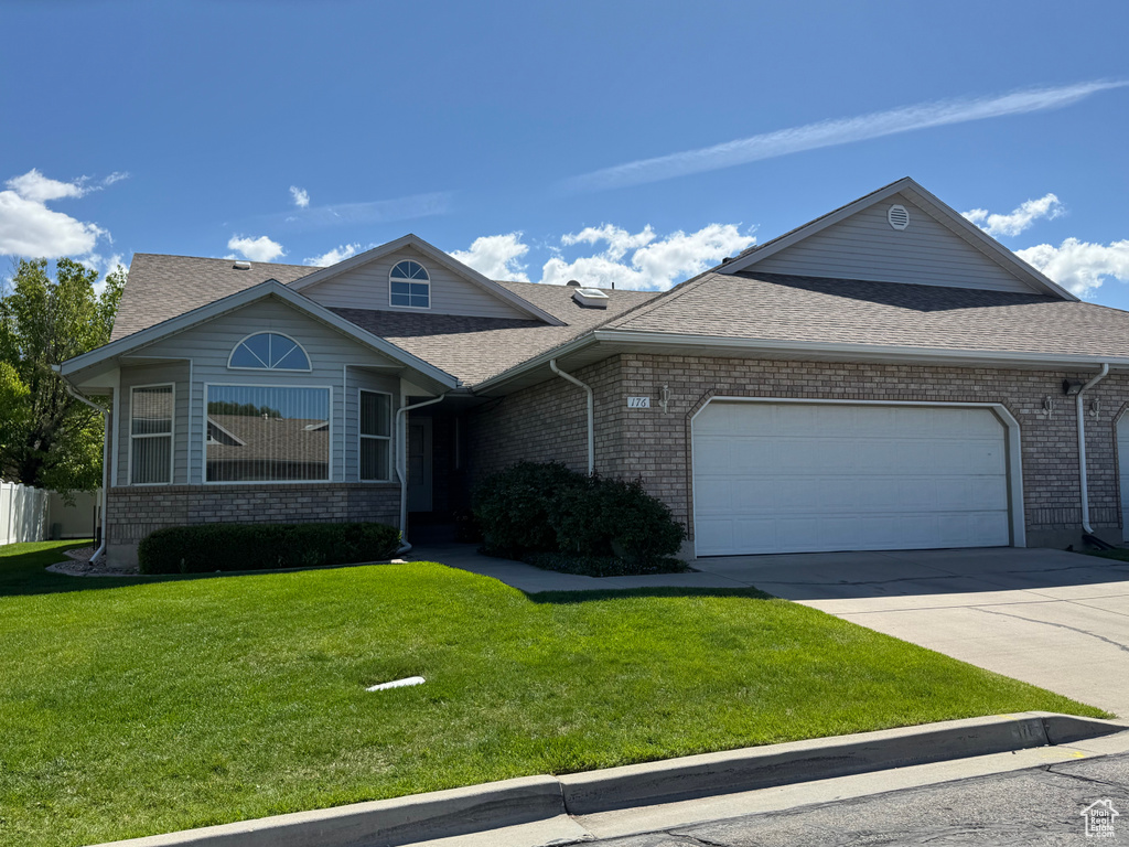 View of front facade featuring driveway, a front yard, brick siding, an attached garage, and a shingled roof
