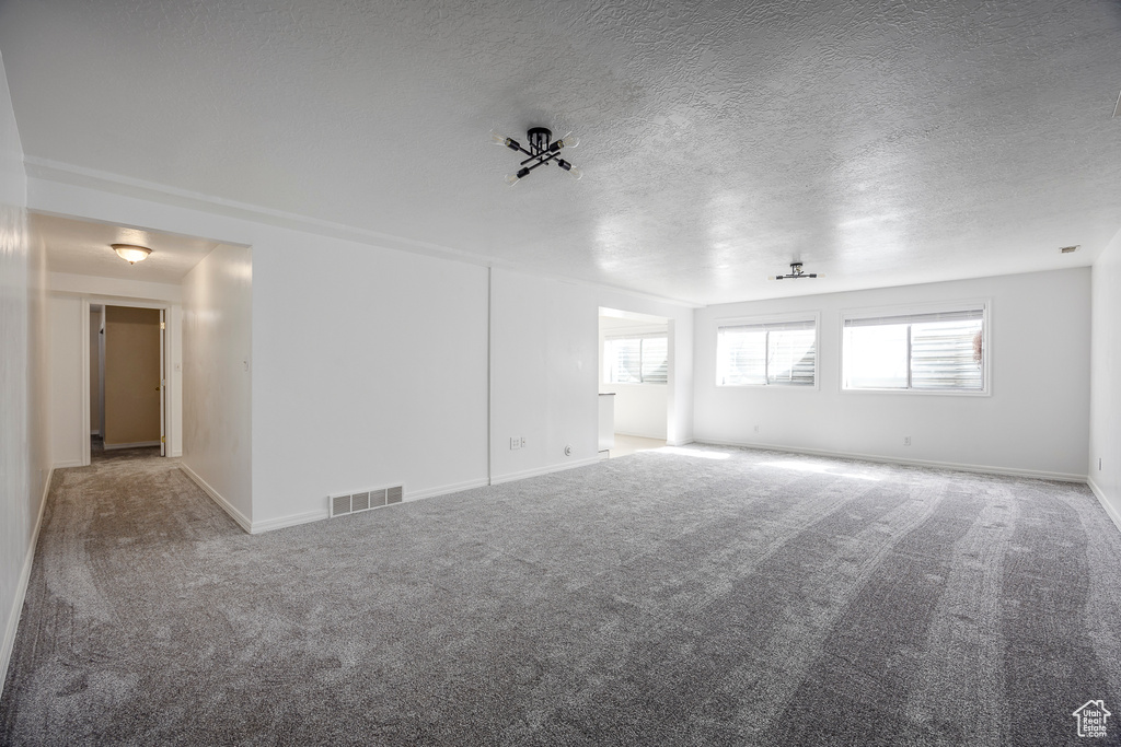 Spare room with carpet floors, a textured ceiling, visible vents, and baseboards