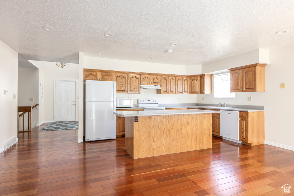 Kitchen with a kitchen island, dark wood-style flooring, a textured ceiling, under cabinet range hood, and white appliances