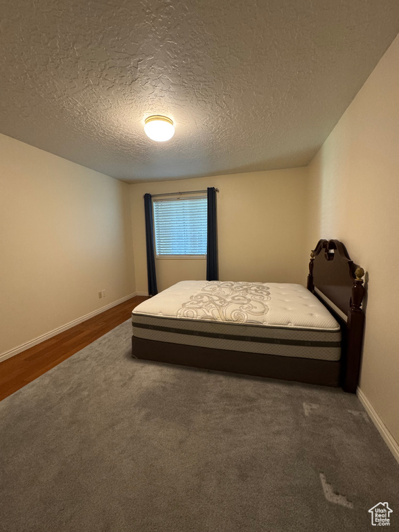 Carpeted bedroom featuring a textured ceiling, baseboards, and wood finished floors
