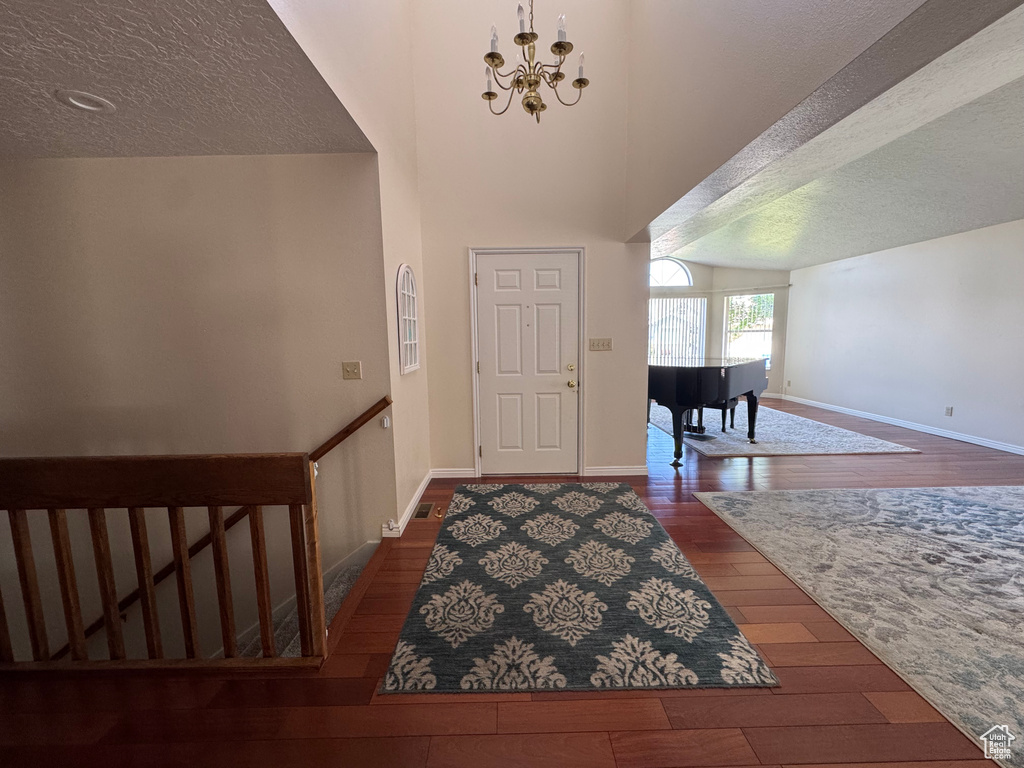 Foyer entrance with wood-type flooring, a textured ceiling, a chandelier, and baseboards