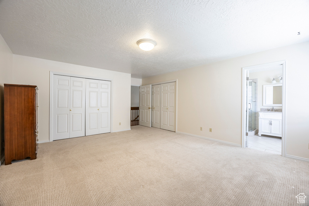 Unfurnished bedroom featuring light colored carpet, a sink, baseboards, multiple closets, and ensuite bathroom