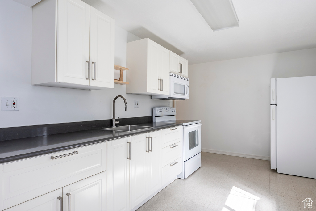 Kitchen with dark countertops, white appliances, light floors, white cabinetry, and a sink
