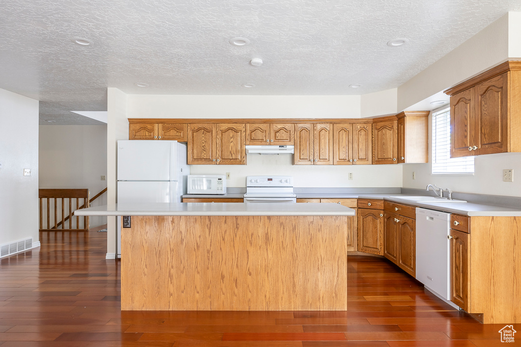 Kitchen featuring visible vents, a kitchen island, white appliances, under cabinet range hood, and a sink