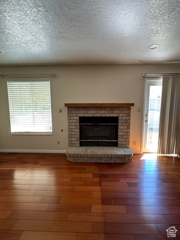Unfurnished living room featuring a brick fireplace, a textured ceiling, plenty of natural light, baseboards, and wood finished floors