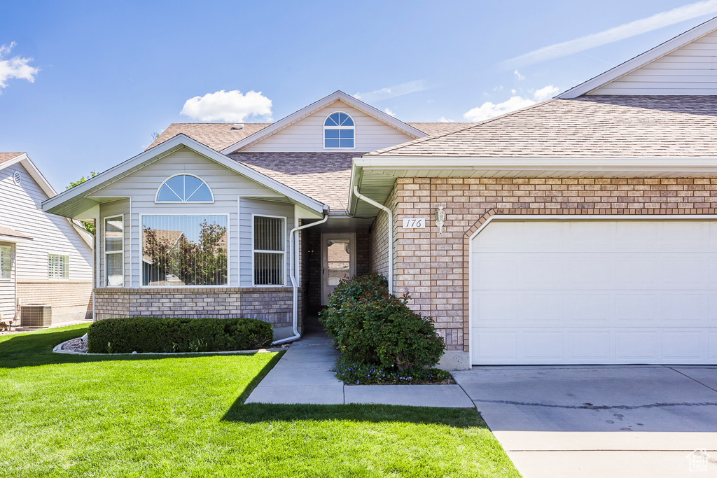 View of front facade featuring a garage, a shingled roof, a front yard, and brick siding