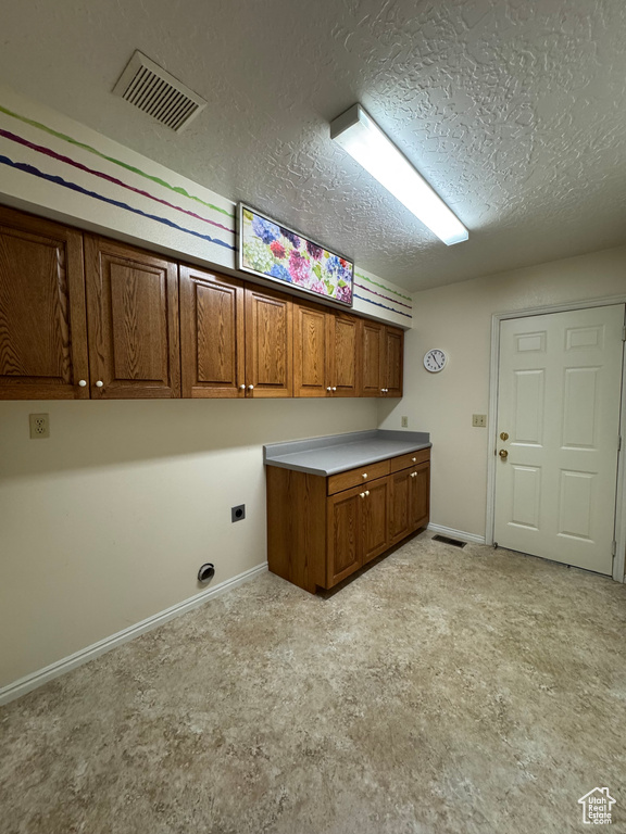 Washroom with cabinet space, electric dryer hookup, a textured ceiling, and visible vents