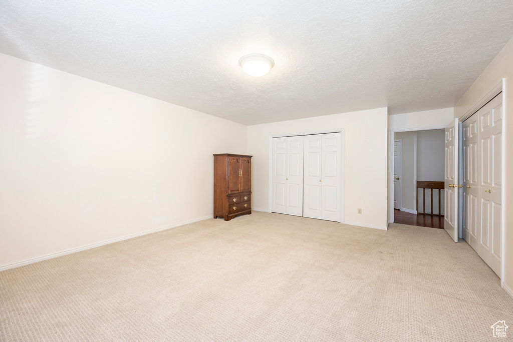 Unfurnished bedroom with baseboards, light carpet, two closets, and a textured ceiling