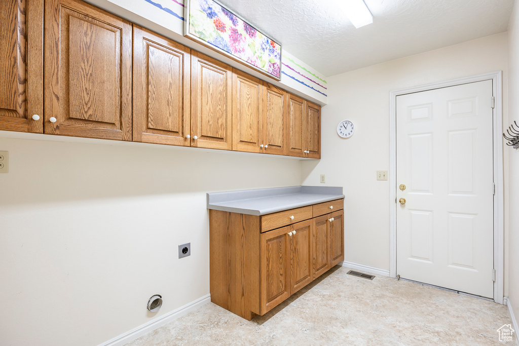 Washroom featuring baseboards, electric dryer hookup, cabinet space, and visible vents