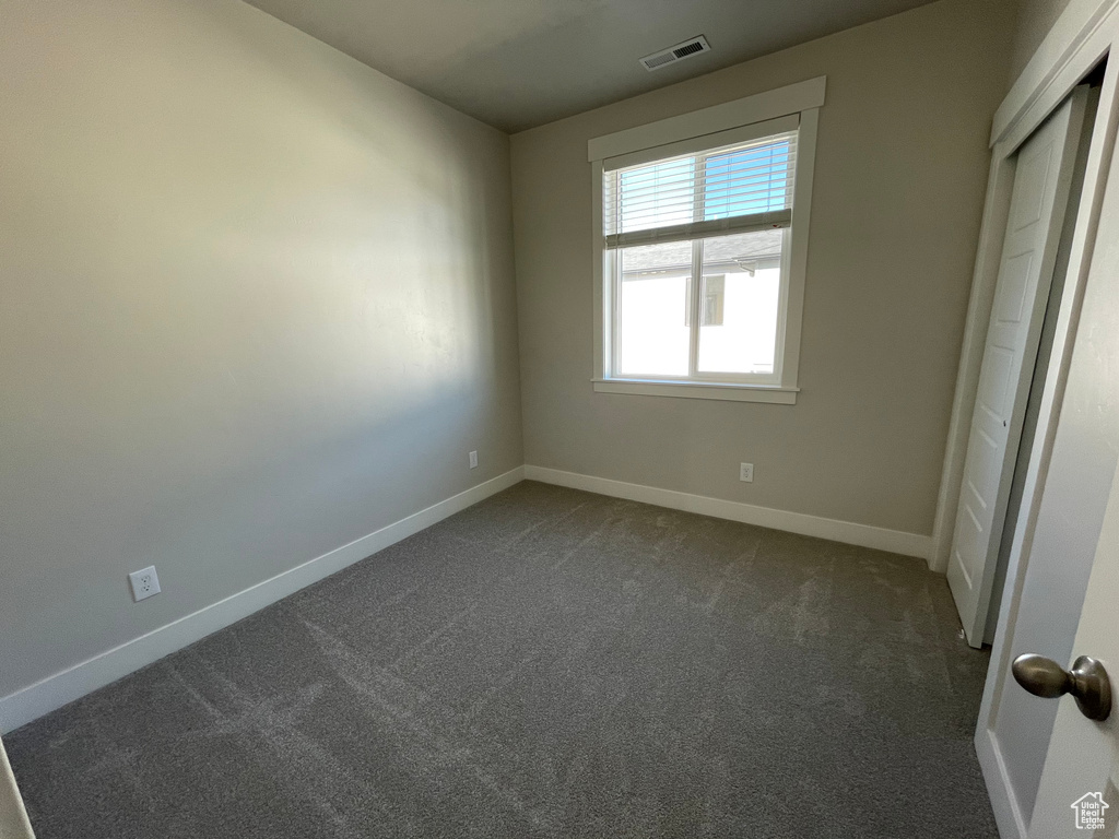 Unfurnished bedroom with dark carpet, baseboards, and a closet