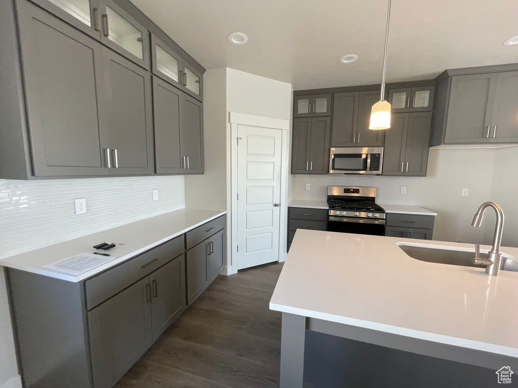 Kitchen featuring appliances with stainless steel finishes, a sink, dark wood-style flooring, tasteful backsplash, and light countertops