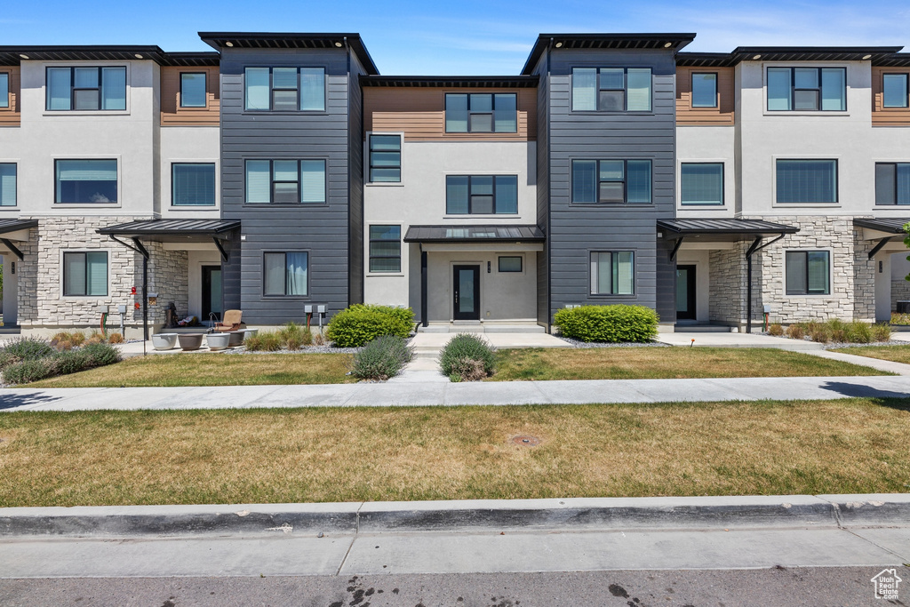Townhome / multi-family property featuring a front yard, metal roof, stone siding, and a standing seam roof