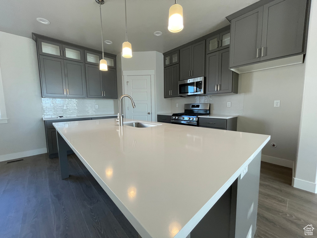 Kitchen featuring stainless steel appliances, a sink, a large island with sink, baseboards, and decorative backsplash