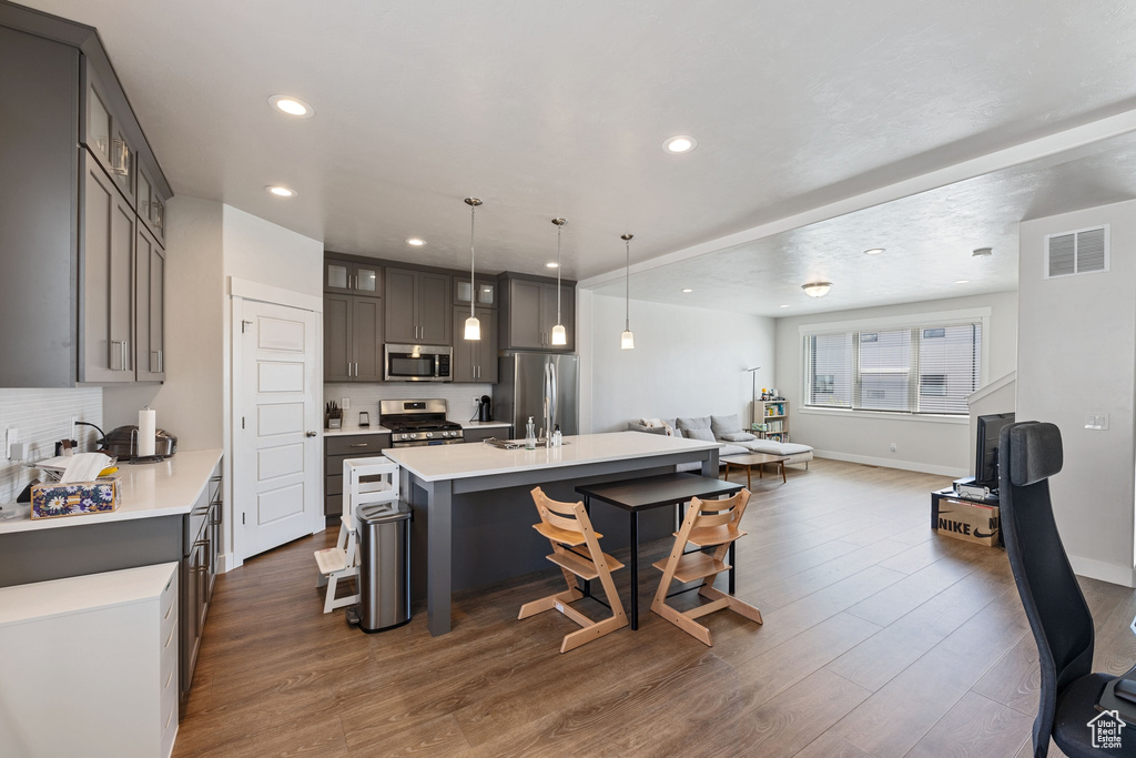 Kitchen featuring appliances with stainless steel finishes, light countertops, an island with sink, open floor plan, and a kitchen bar