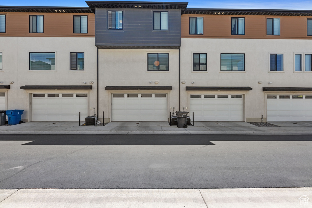 Exterior space with an attached garage, cooling unit, and stucco siding