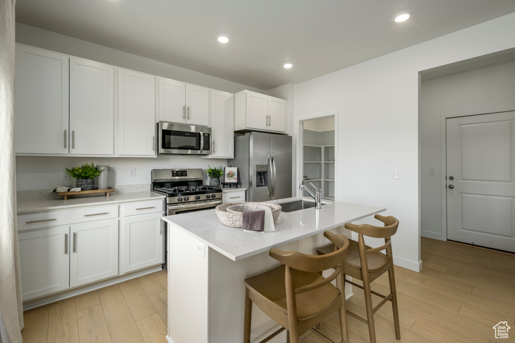 Kitchen featuring stainless steel appliances, white cabinetry, a sink, and light wood-style floors