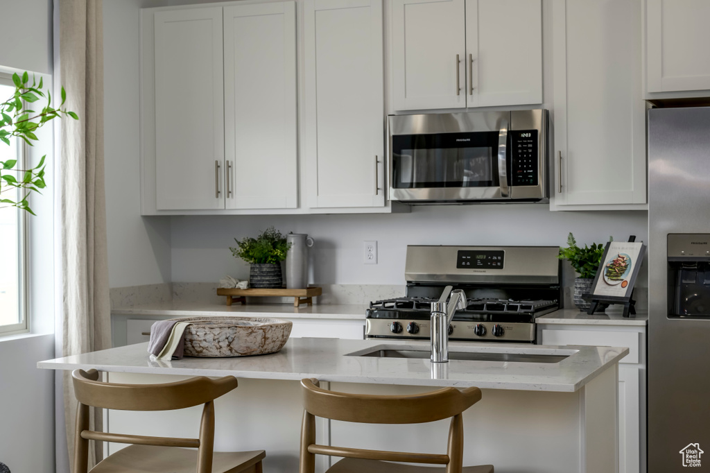 Kitchen with white cabinets, appliances with stainless steel finishes, and a kitchen bar