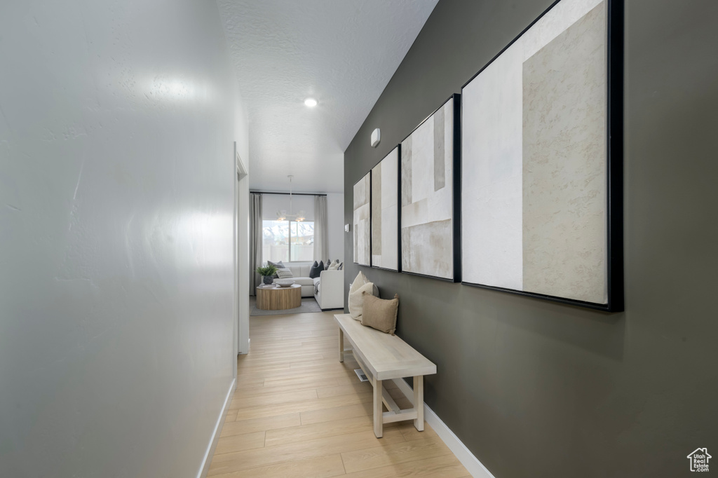 Hallway featuring an inviting chandelier, baseboards, and light wood finished floors