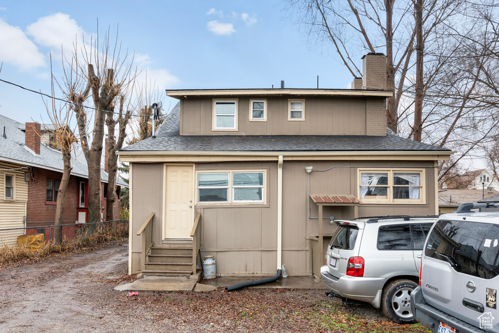 View of front facade featuring fence, a chimney, a shingled roof, and entry steps