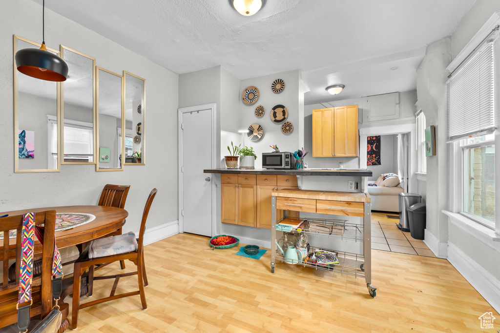 Kitchen with light brown cabinetry, baseboards, stainless steel microwave, and light wood-style flooring