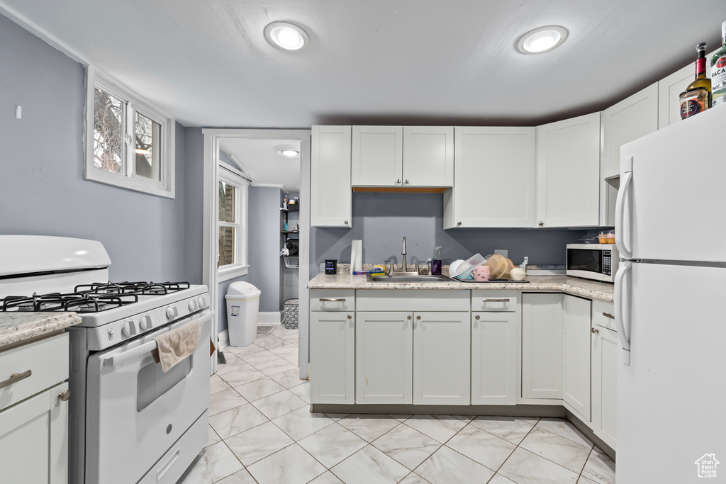 Kitchen featuring a sink, light stone countertops, white appliances, and white cabinetry