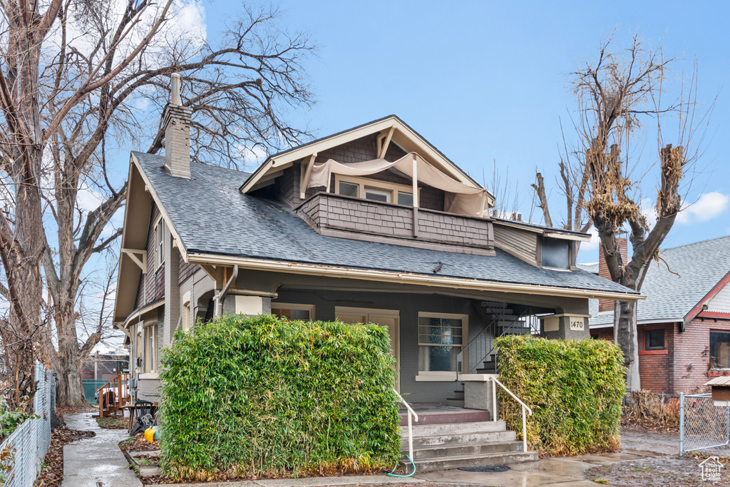 Bungalow-style house featuring a porch, a chimney, fence, a balcony, and a shingled roof