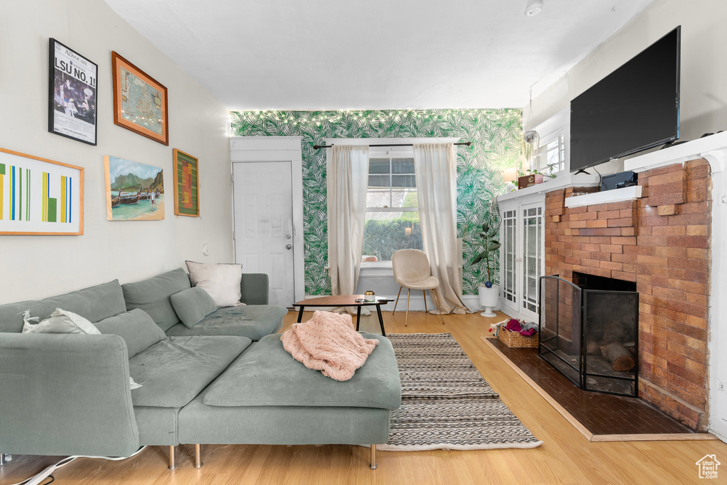 Living area with a brick fireplace, wallpapered walls, and wood finished floors