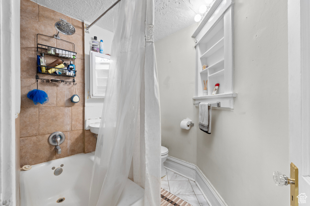 Bathroom featuring baseboards, marble finish floor, a textured ceiling, and toilet