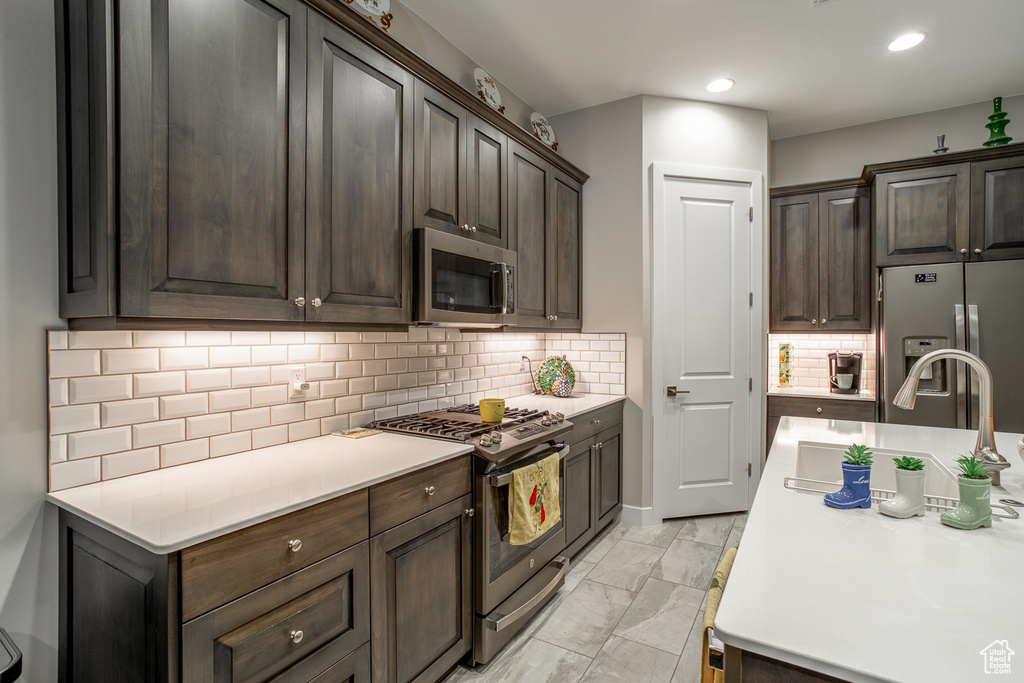 Kitchen with light countertops, appliances with stainless steel finishes, dark brown cabinets, and marble finish floor