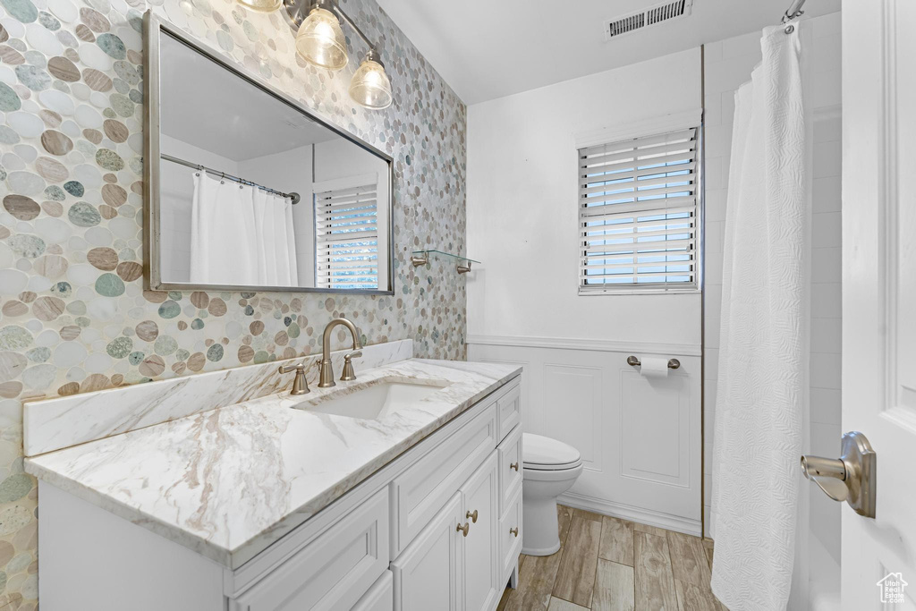 Full bathroom with wallpapered walls, visible vents, wainscoting, and a wealth of natural light