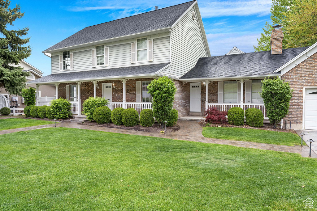 View of front of home with a shingled roof, a front yard, a porch, and brick siding