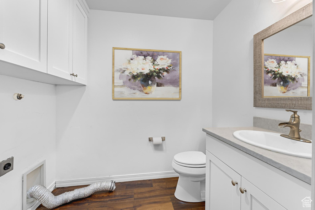 Half bathroom with vanity, baseboards, toilet, and wood finished floors