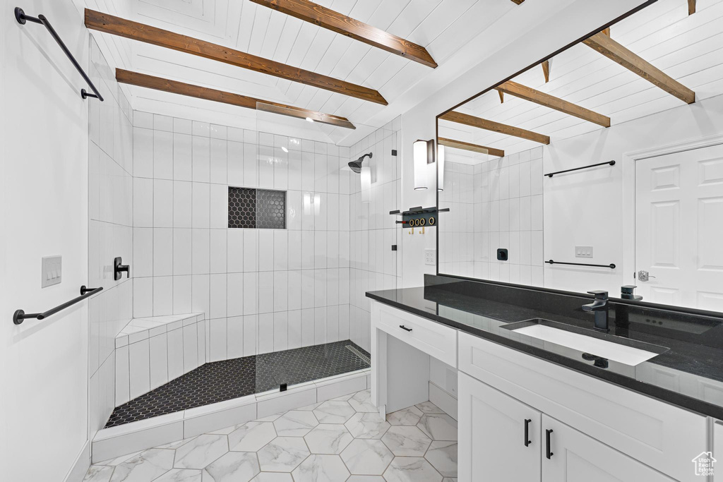Full bath featuring vanity, tile patterned flooring, a tile shower, and beamed ceiling