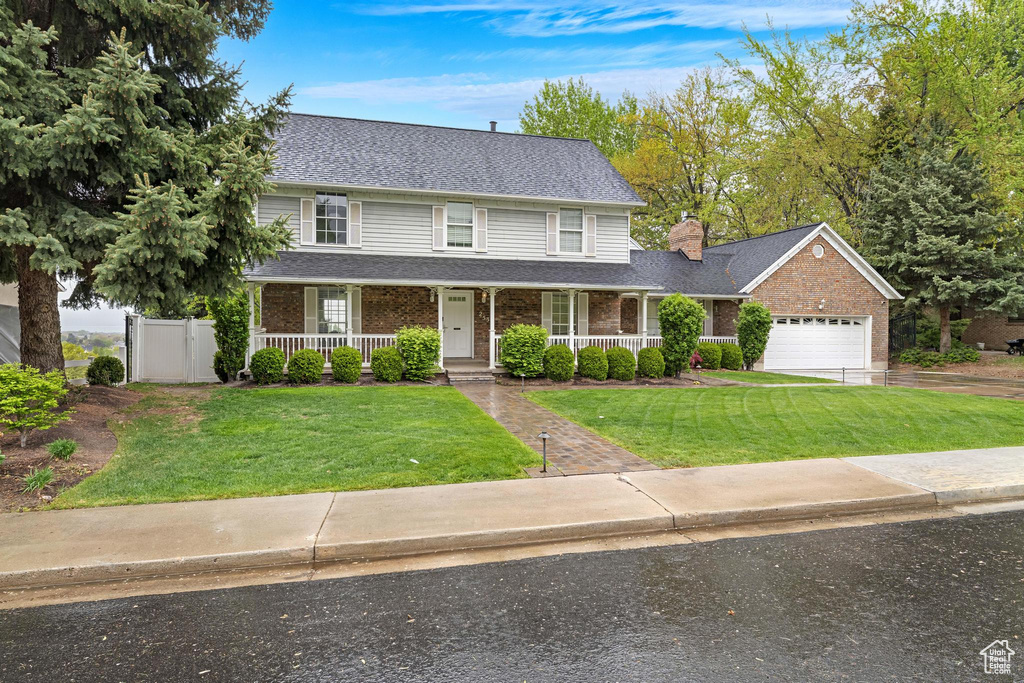 View of front facade with covered porch, a front yard, brick siding, an attached garage, and a shingled roof